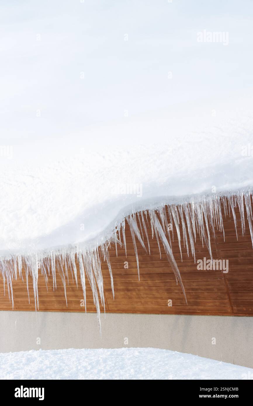 Large icicles hanging from a building roof in covered in white winter snow Stock Photo
