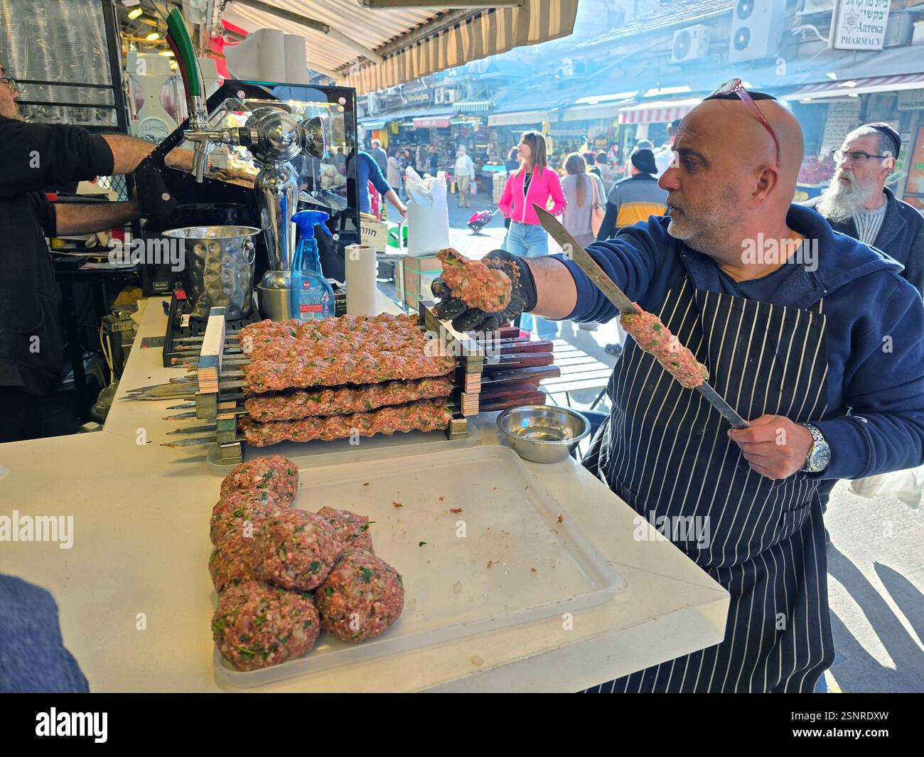 A cook expertly shapes seasoned meat for skewering amidst the lively atmosphere at the Mahane Yehuda market in Jerusalem, Israel. - Smartphone Captured Stock Image