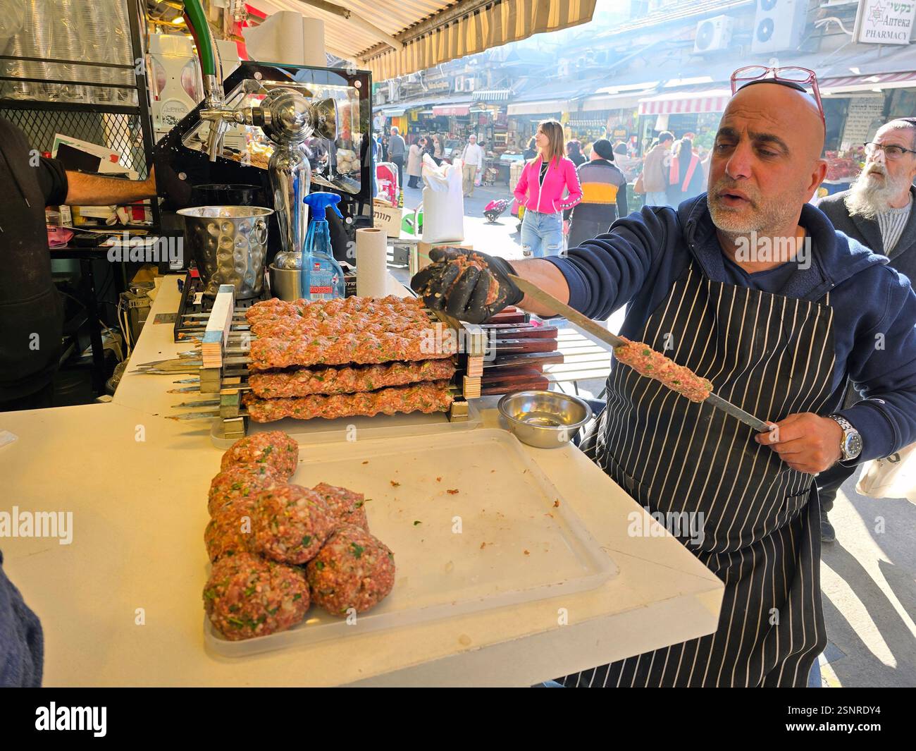 A cook expertly shapes seasoned meat for skewering amidst the lively atmosphere at the Mahane Yehuda market in Jerusalem, Israel. - Smartphone Captured Stock Image