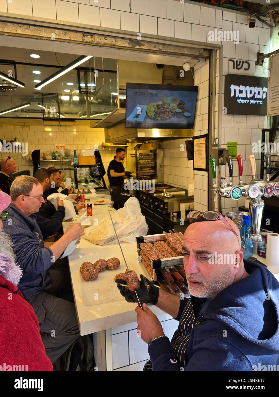 A cook expertly shapes seasoned meat for skewering amidst the lively atmosphere at the Mahane Yehuda market in Jerusalem, Israel. - Smartphone Captured Stock Image