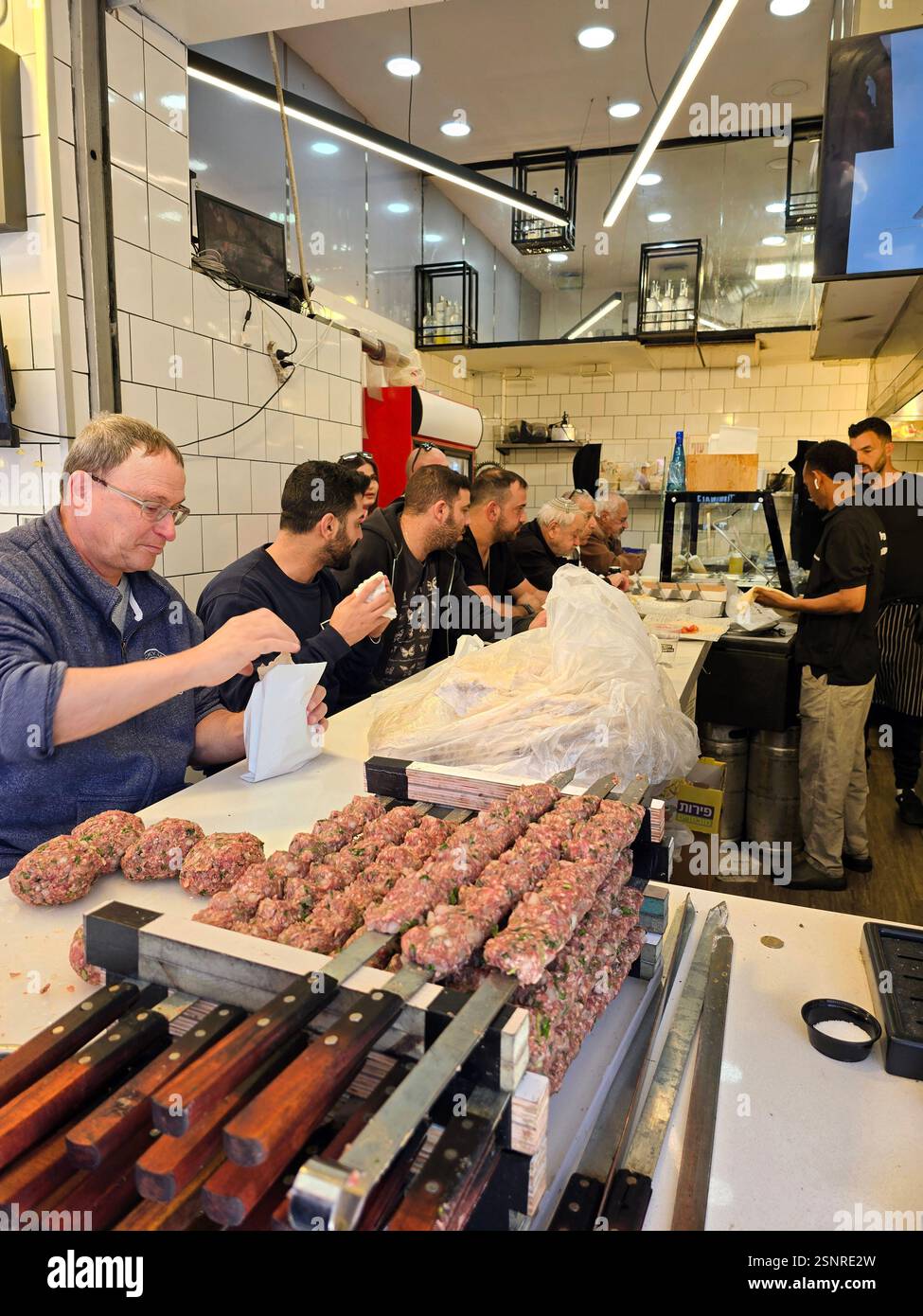 A cook expertly shapes seasoned meat for skewering amidst the lively atmosphere at the Mahane Yehuda market in Jerusalem, Israel. - Smartphone Captured Stock Image