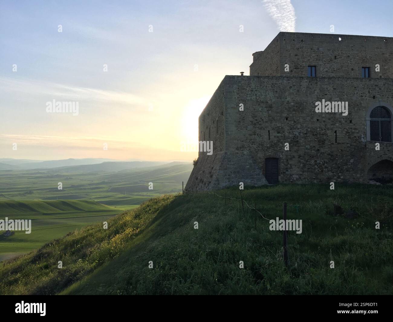 An ancient stone castle in Monteserico (Genzano - Italy) stands on a hill as the sun sets, casting a warm glow over the lush green landscape of rollin Stock Photo
