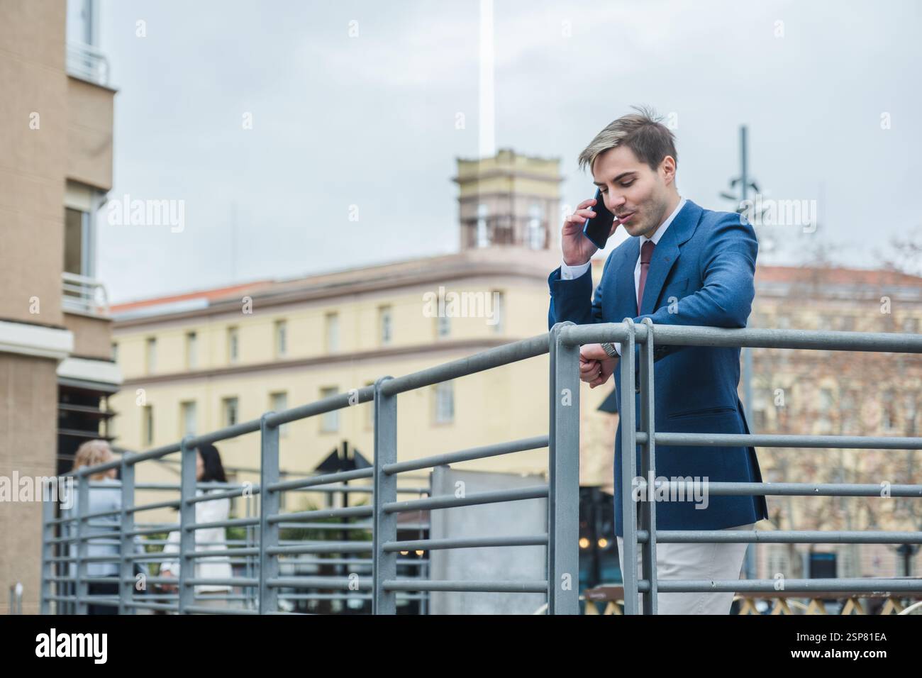 Businessman checking time while talking on phone in urban setting Stock Photo