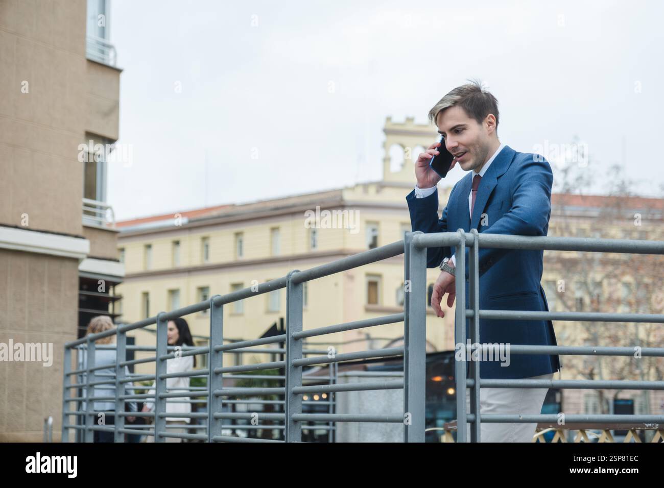 Businessman leaning on railing and talking on smartphone in city Stock Photo