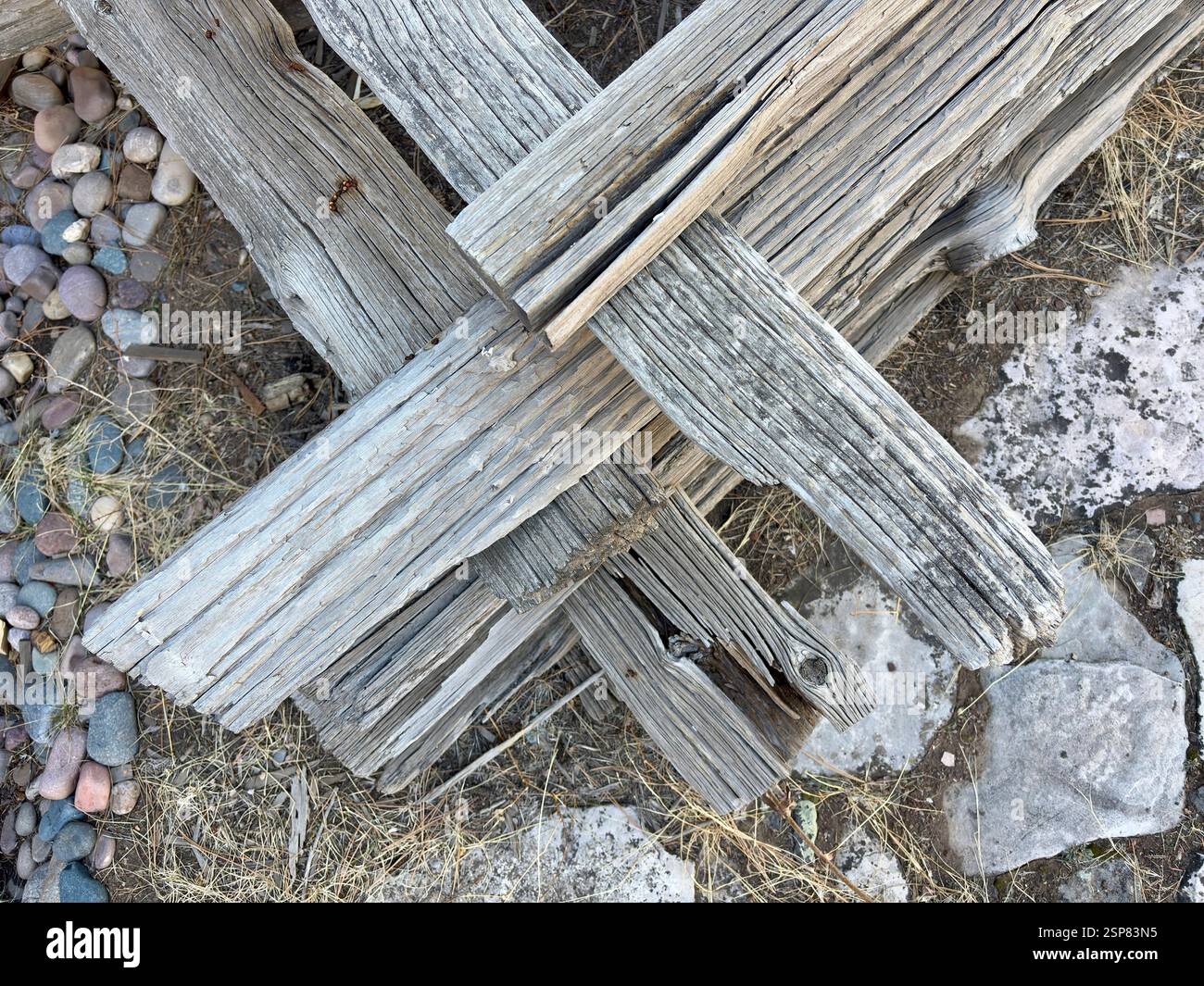 Intersecting weathered wooden beams on dry ground with rocks and grass ...
