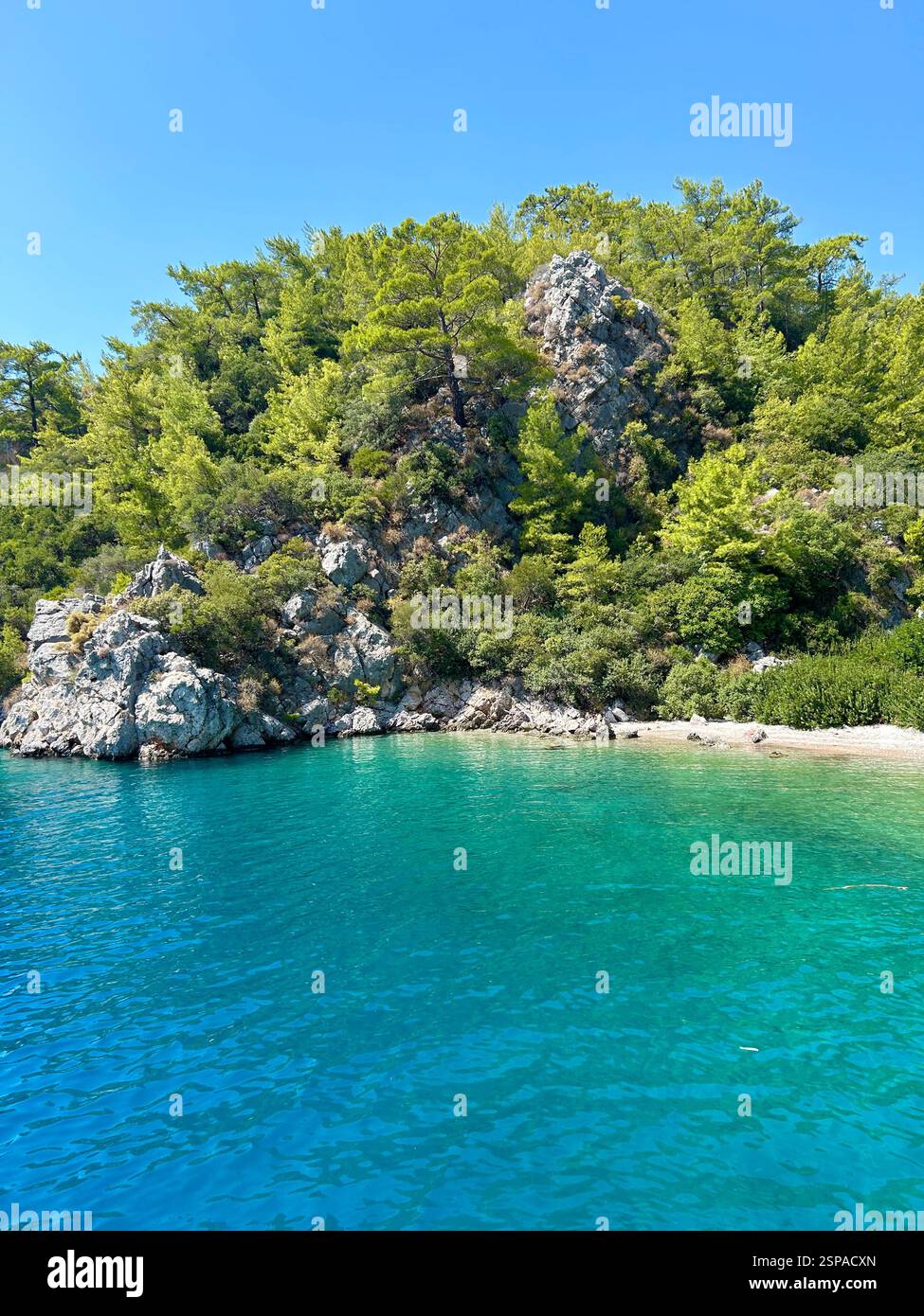 The crystal clear blue waters of the Mediterranean Sea against the mountains and trees - Smartphone Captured Stock Image