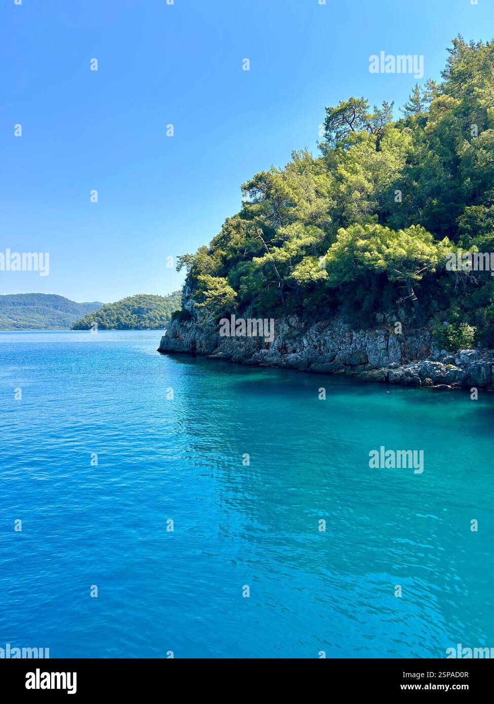 The crystal clear blue waters of the Mediterranean Sea next to mountains and trees - Smartphone Captured Stock Image