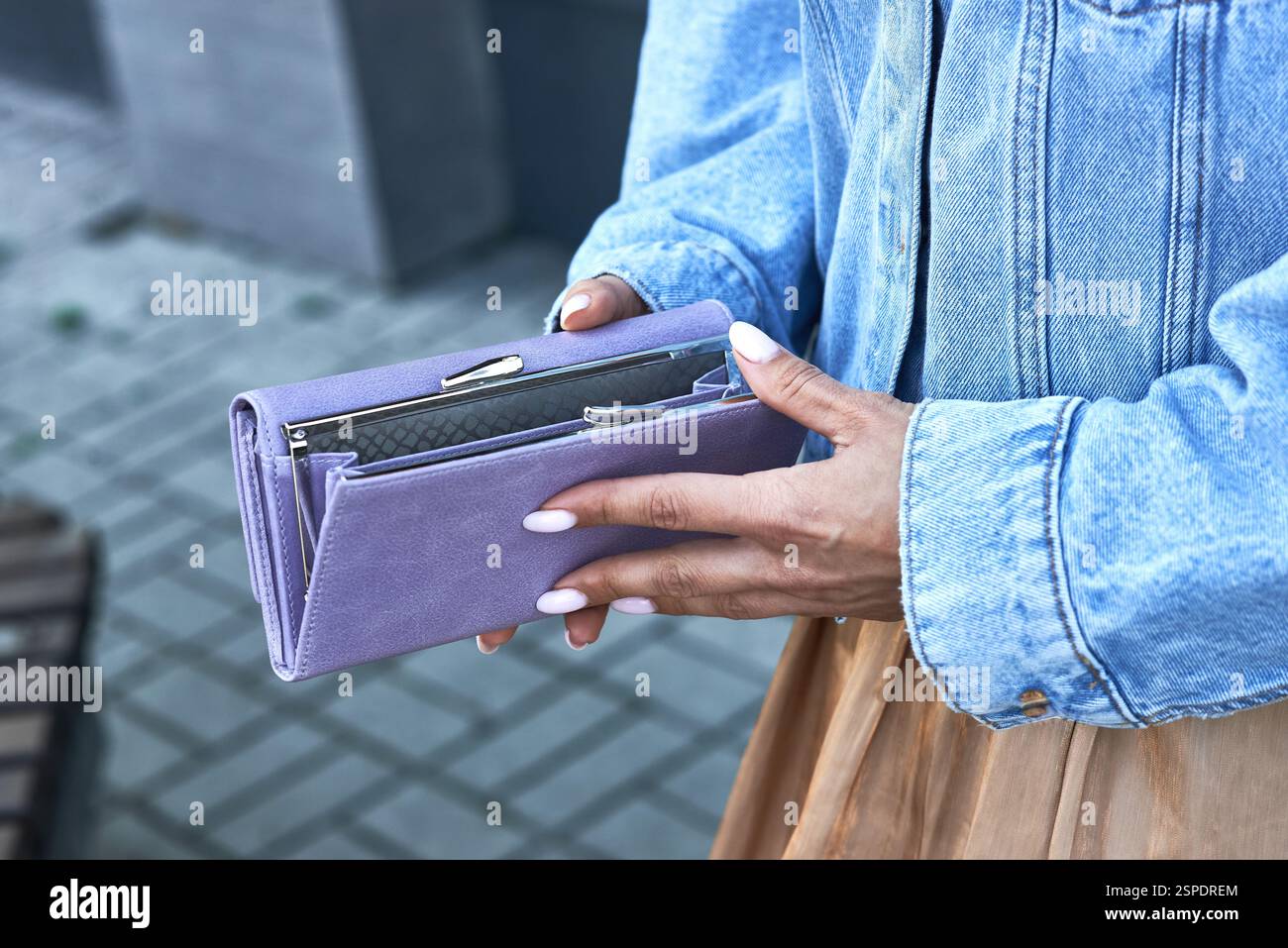 Woman holding stylish lavender wallet in denim jacket, highlighting a modern fashion accessory, city background outdoors, fashion style concept Stock Photo