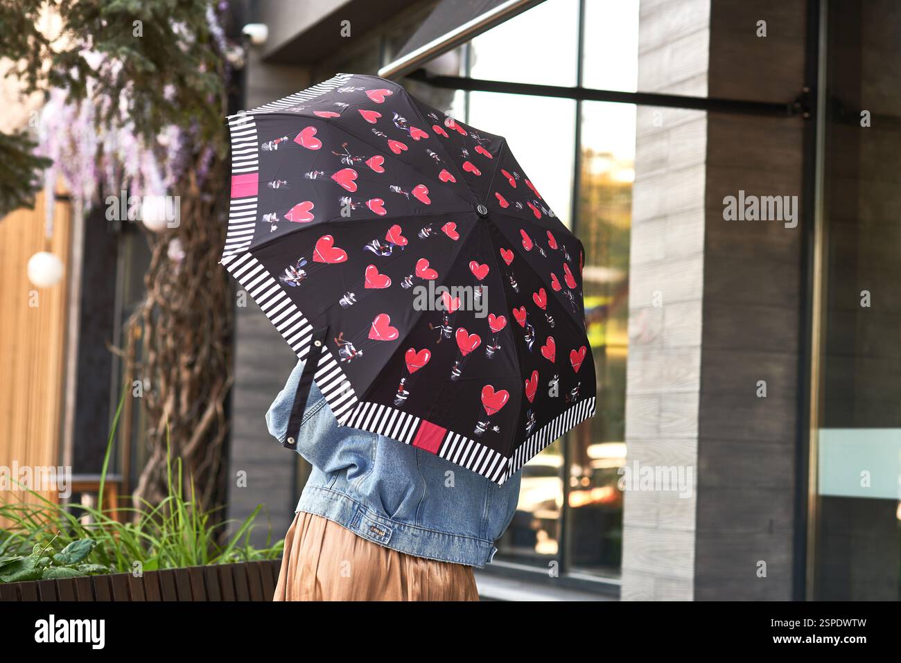 In an urban setting, a trendy fashion accessory is shown as a stylish person holds a heart-patterned umbrella, rainy day concept Stock Photo