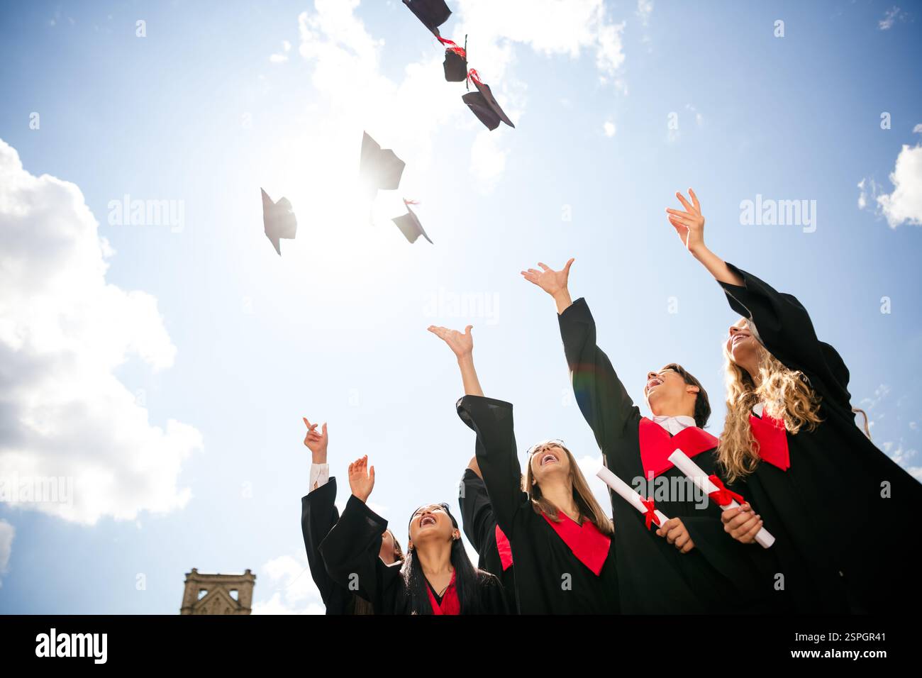 Graduating students celebrate by tossing caps in bright sunny sky ...