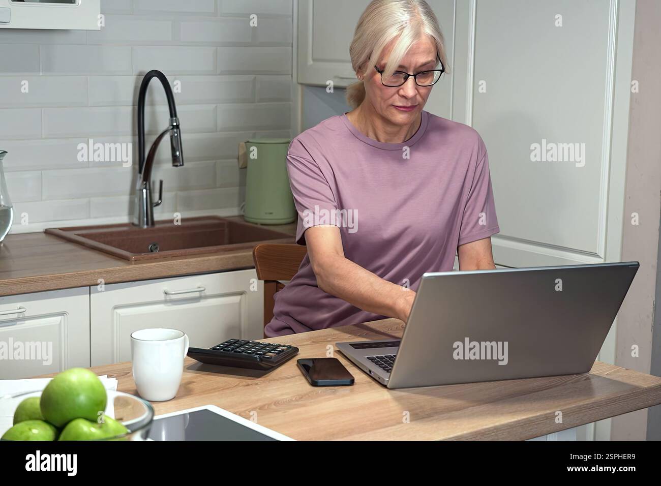 Elderly woman typing on laptop and calculator Stock Photo