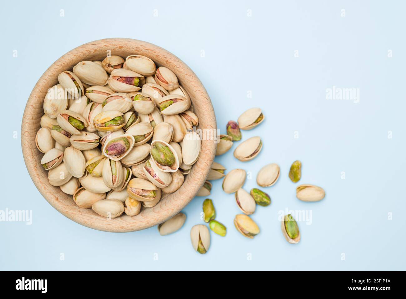 Pistachio nuts into wooden bowl on light blue background. Top view. Stock Photo