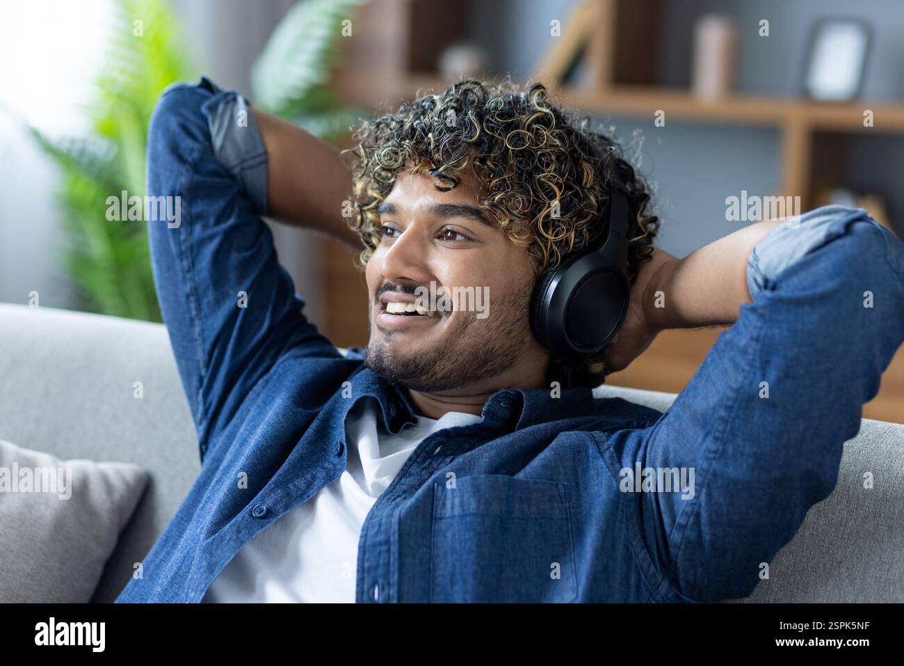 A man is resting listening to music, sitting on a sofa with headphones ...
