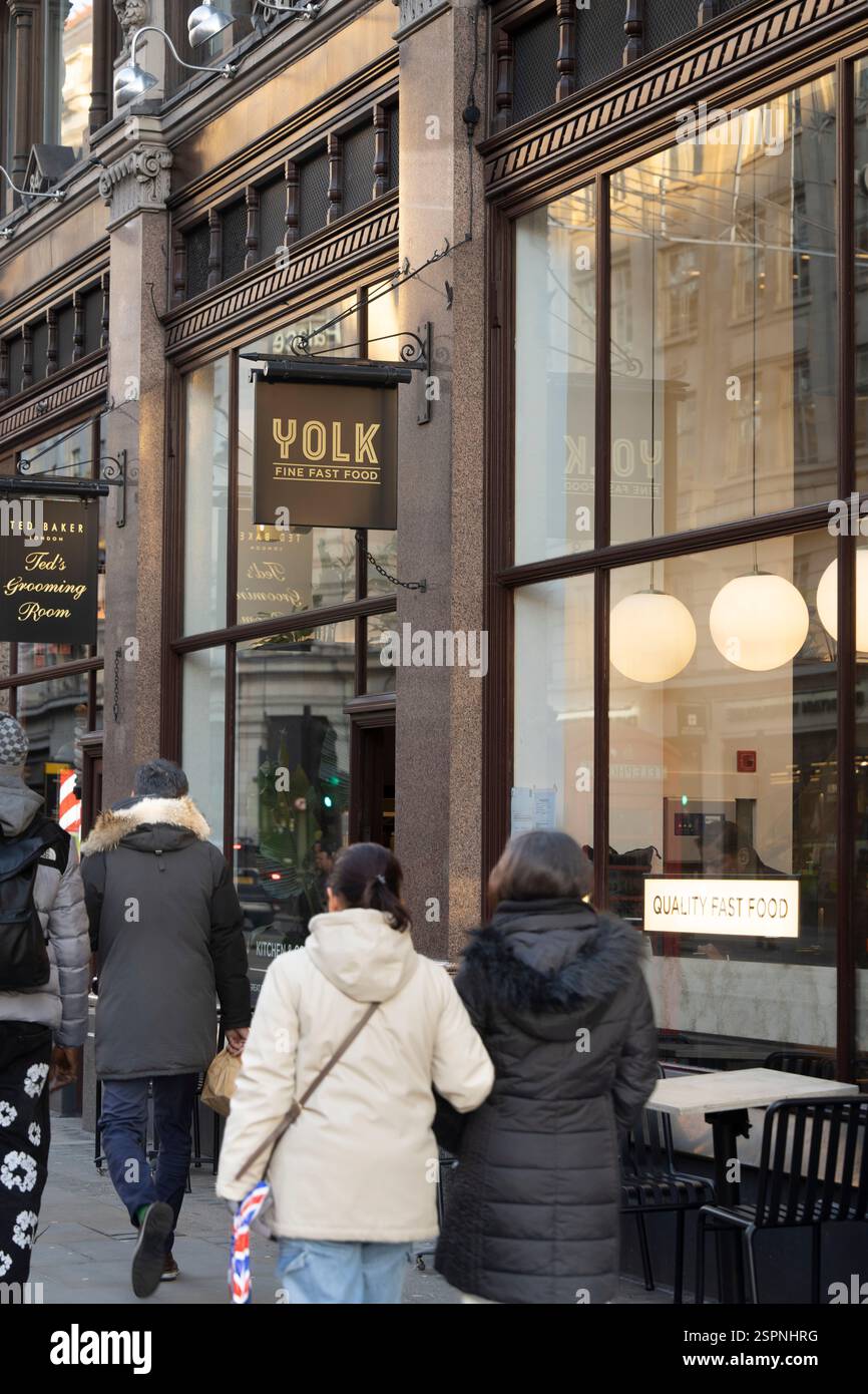 Pedestrians walk past Yolk, a fine fast food restaurant, on Strand, London, near Ted's Grooming Room. Stock Photo