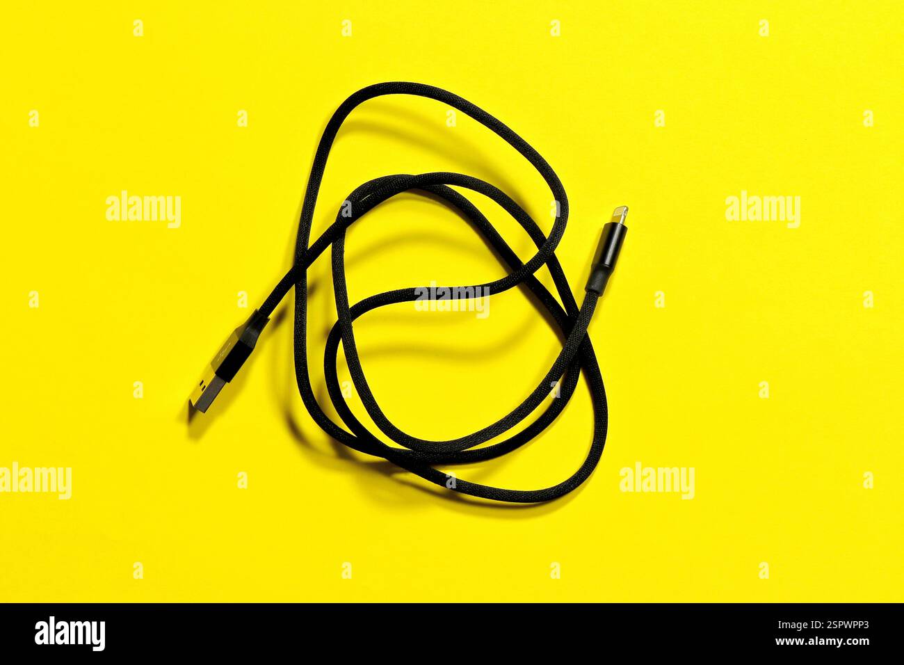 Black usb iPhone charging cable, coiled in a ring, on a yellow background. Stock Photo