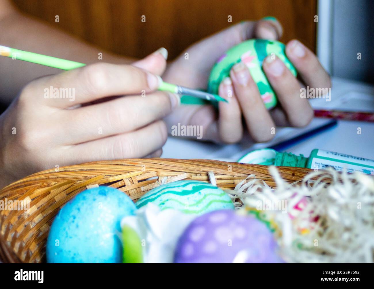 Colorful Easter eggs in foreground. Hands decorating eggs for Easter holidays. Stock Photo