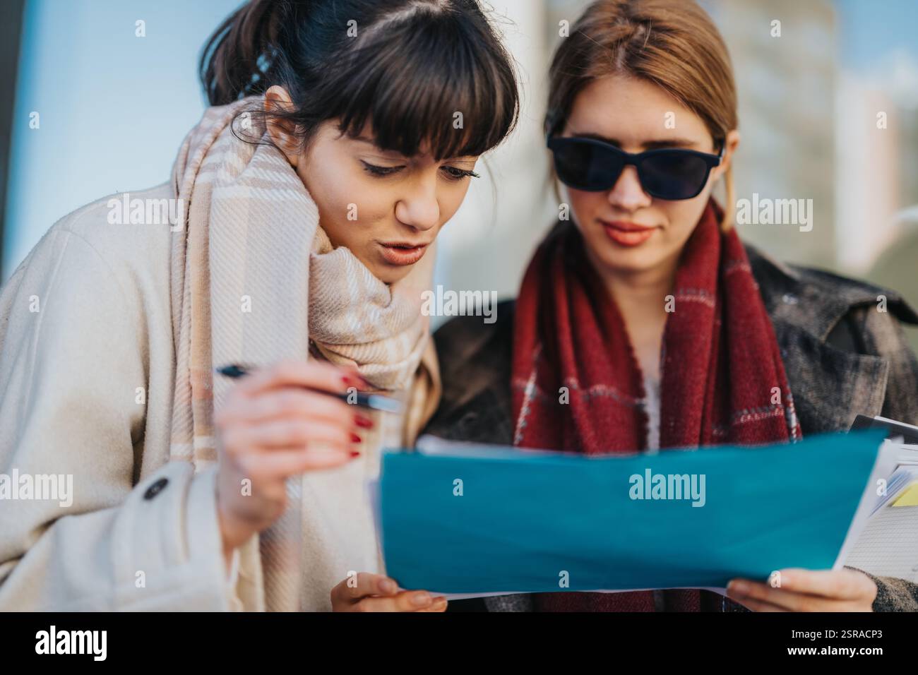Two women collaborating on a project while reviewing documents outdoors Stock Photo