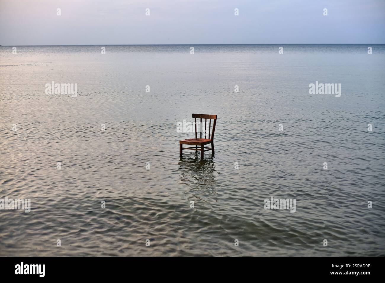 Wooden chair stands in calm, vast ocean, symbolizing solitude and ...