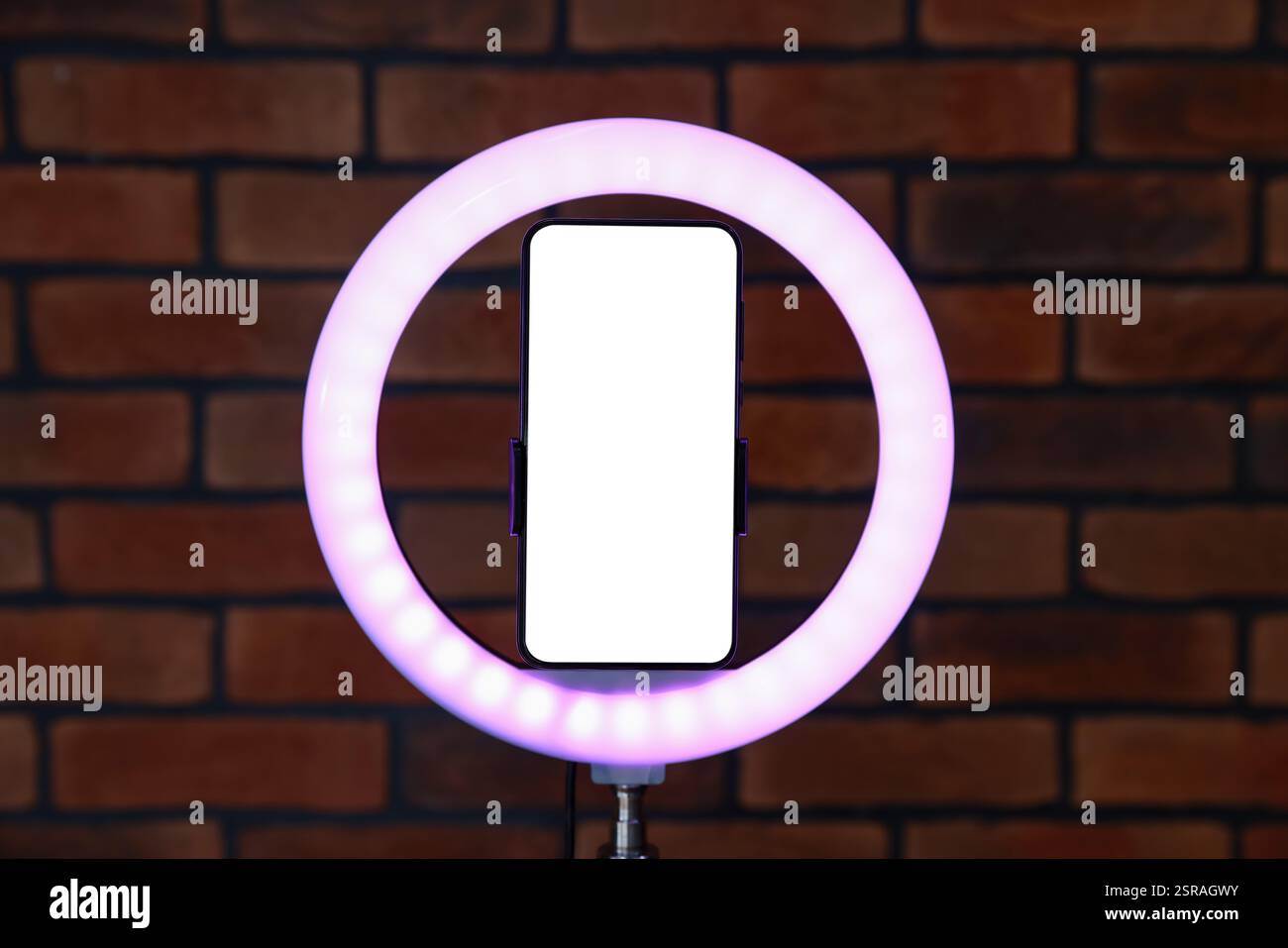 Ring lamp with smartphone against brick wall Stock Photo