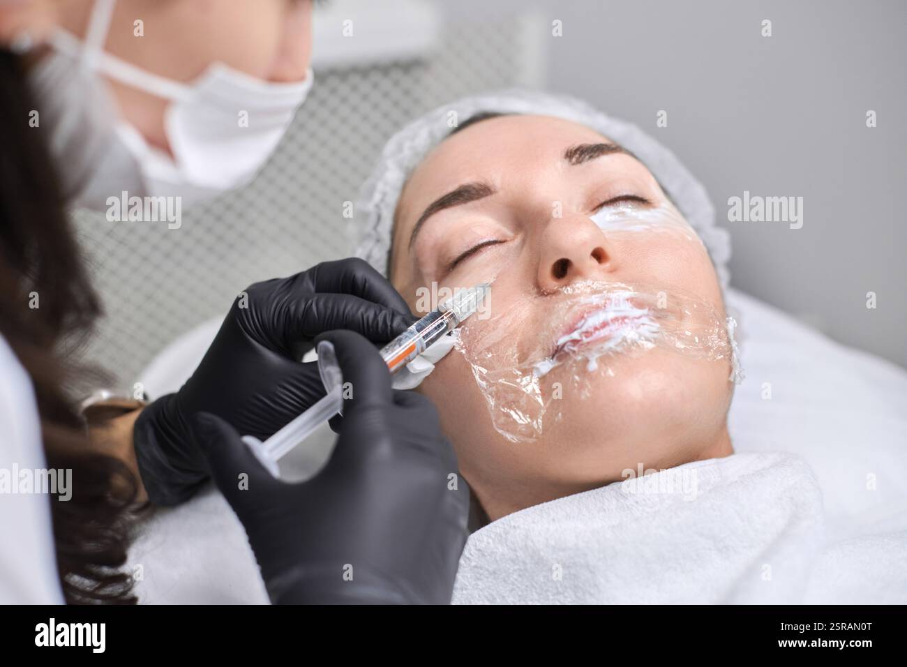Young woman receives facial injection from professional wearing gloves ...