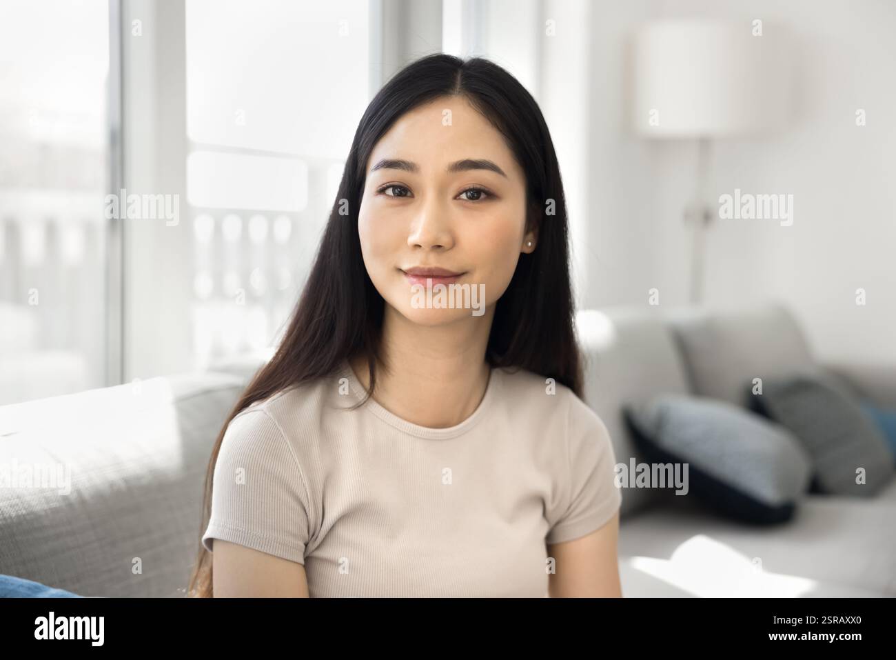 Pretty Asian young woman sitting in cozy, well-lit room Stock Photo