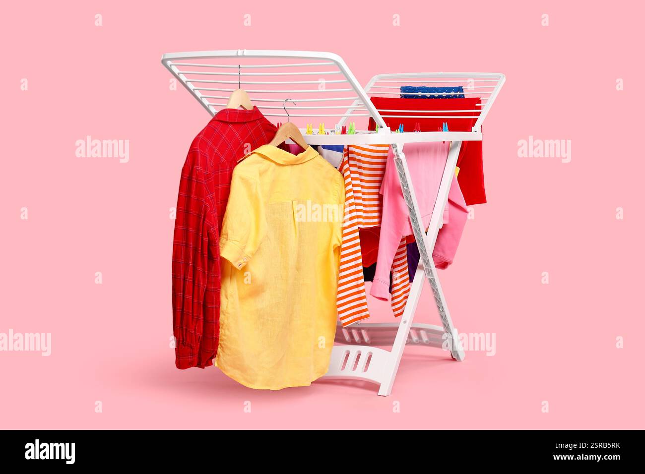 Drying rack with fresh clean laundry on light pink background Stock Photo
