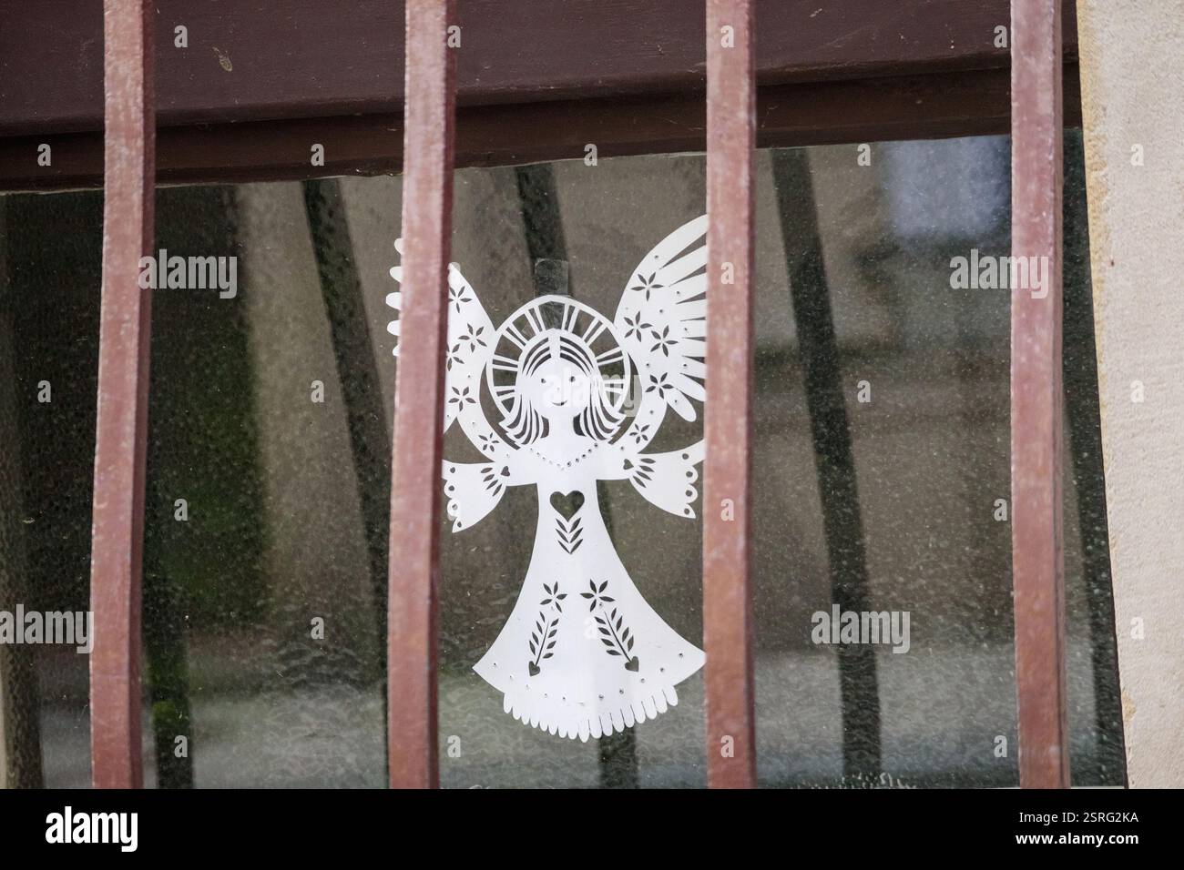 a window with metal bars behind which a decorative paper angel can be seen. Stock Photo