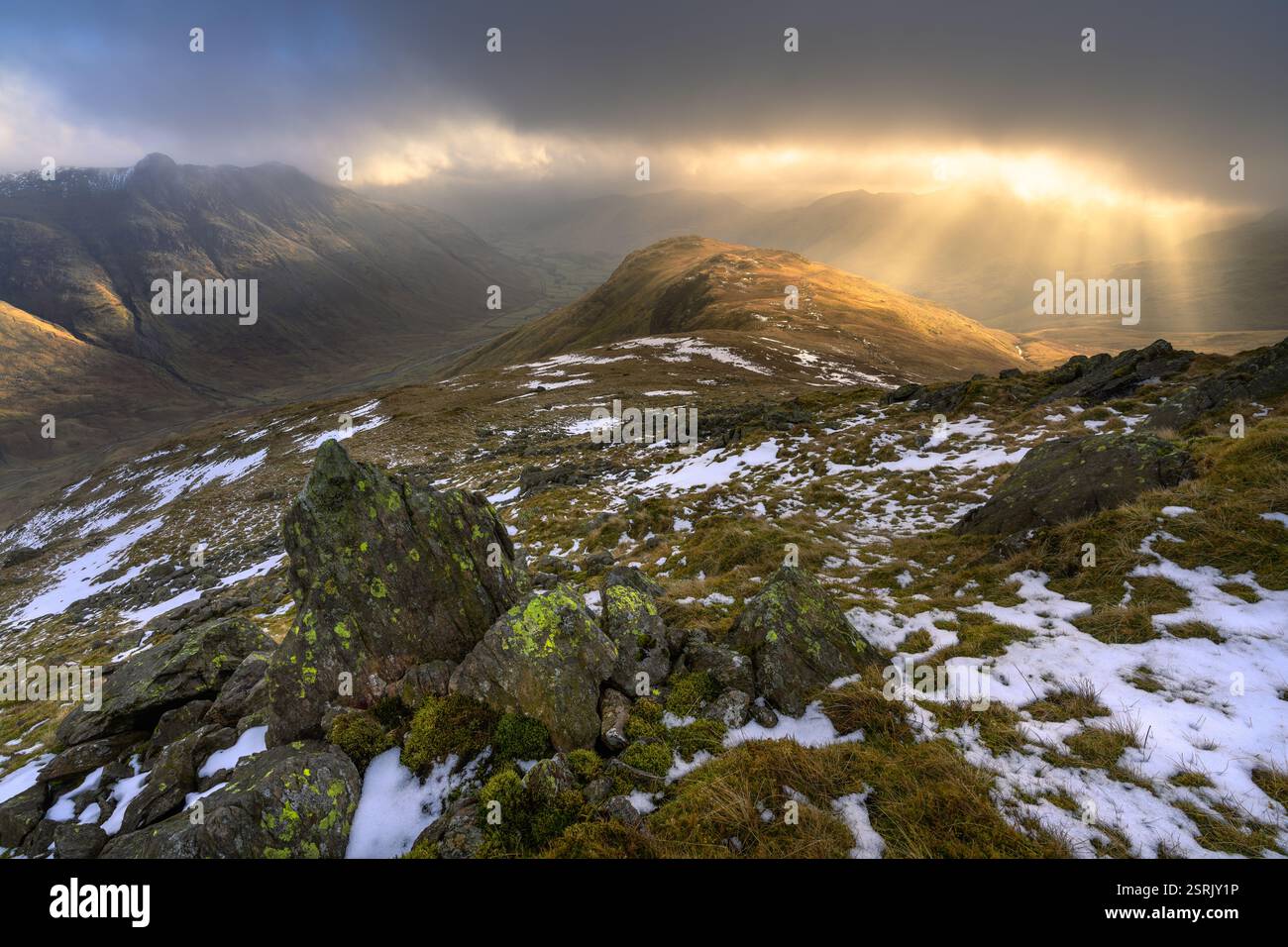 Golden sunrise over Lake District mountains with dark dramatic clouds over The Langdale Valley. Stock Photo