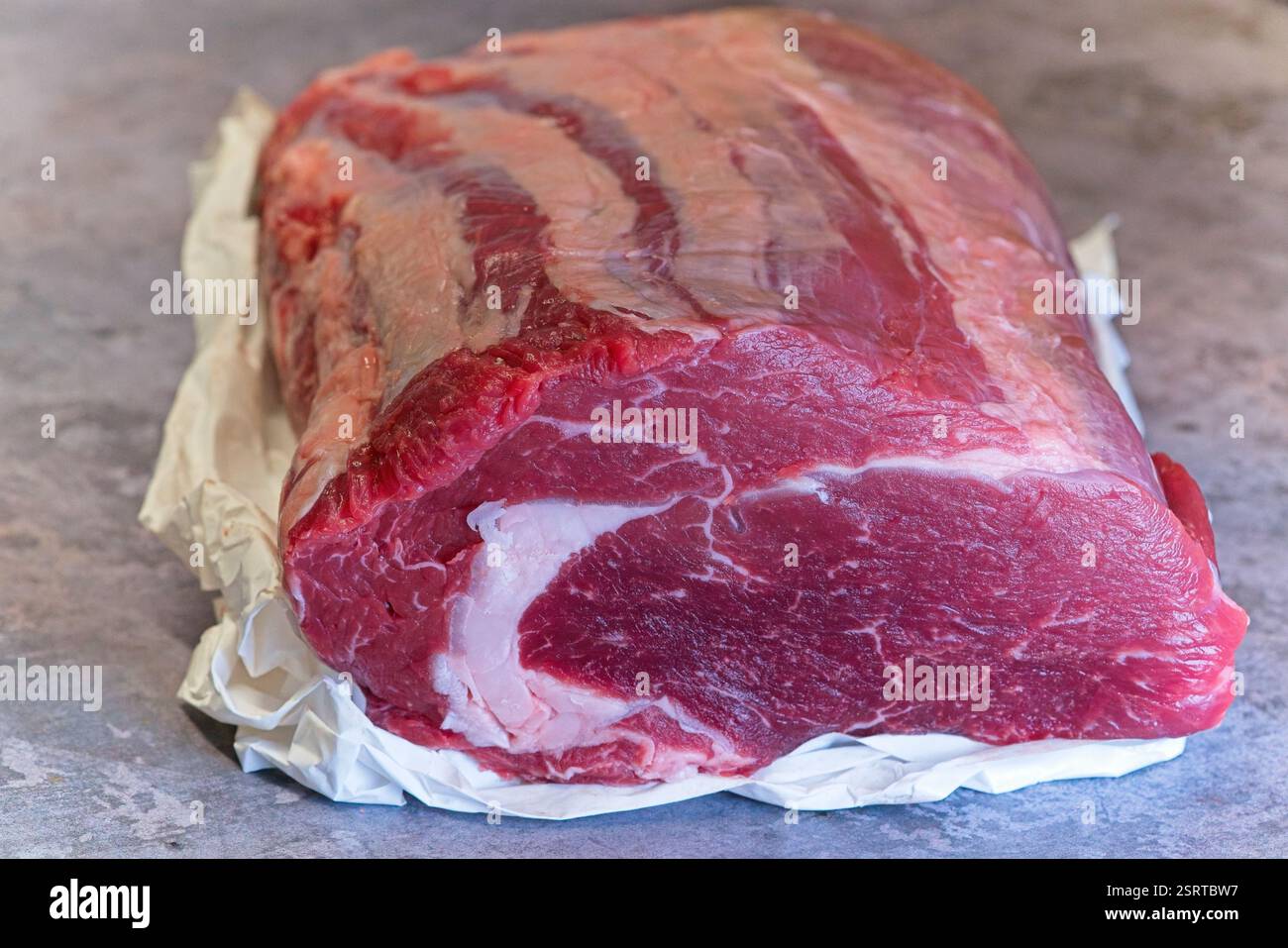 A whole, fresh, raw beef ribeye joint sits, with details showing a fat ...