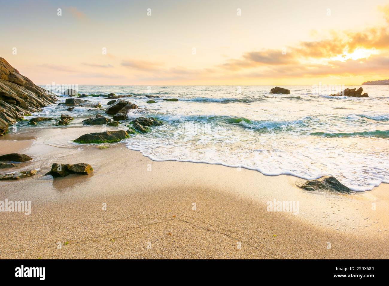 summer holiday season at the seaside. beautiful seascape at sunrise. golden sandy beach in morning light. sun behind fluffy clouds on sky above horizo Stock Photo