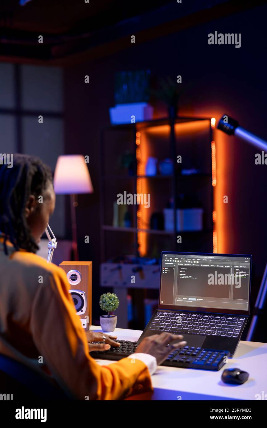 Computer scientist writes code on laptop screen while in apartment office using Java programming languages. African american teenager remotely working on fixing database errors Stock Photo
