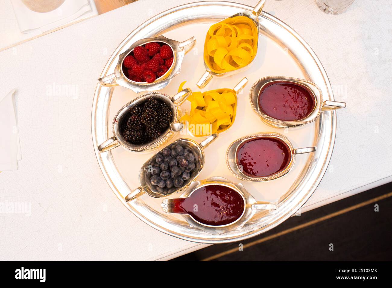 Assorted berries and sauces on a silver tray  A display of raspberries, blackberries, blueberries, and fruit sauces. Stock Photo