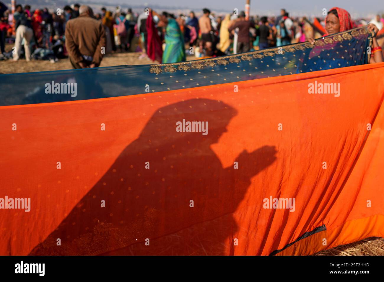 The shadow of a pilgrim falls on a sari held up to dry at the ...