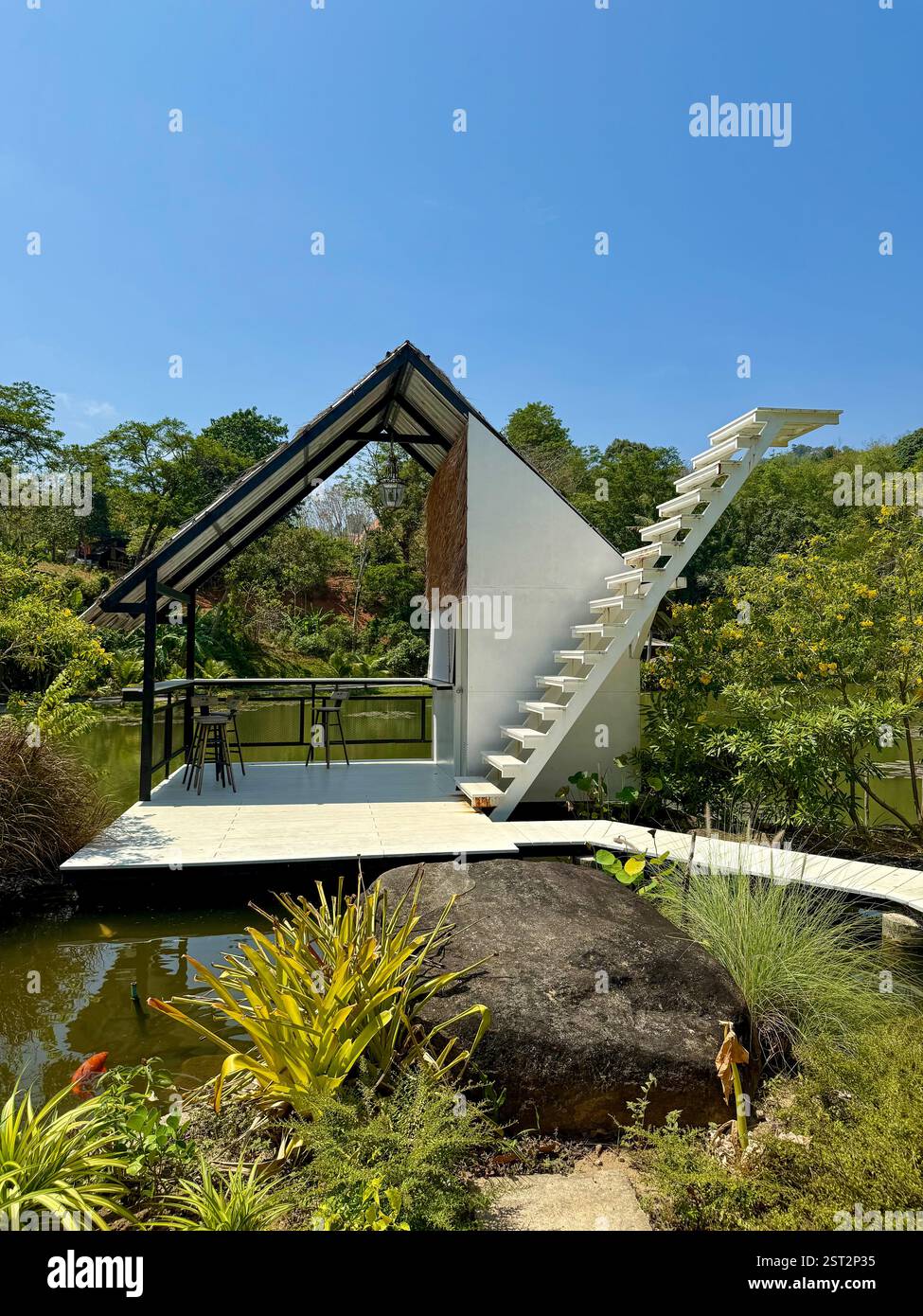 Modern Stilt House by a Tranquil Pond A contemporary small house with a slanted roof and a stilted terrace, located by a calm pond surrounded by lush - Smartphone Captured Stock Image