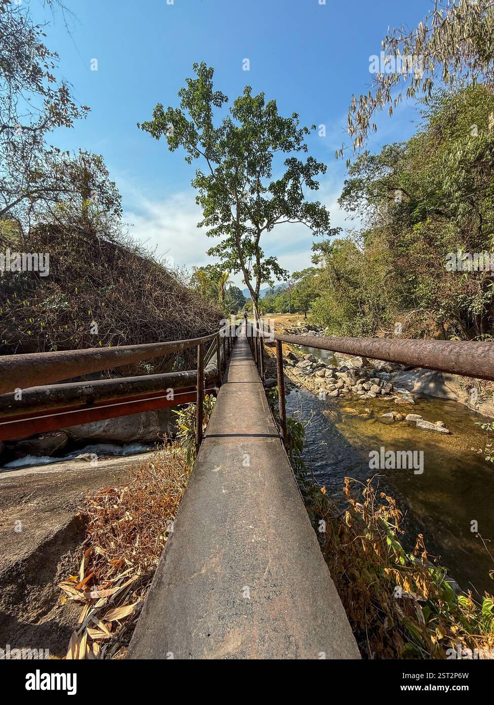 Metal footbridge over a river in the wilderness  A suspended metal footbridge over a river, surrounded by lush vegetation and wild hills. - Smartphone Captured Stock Image