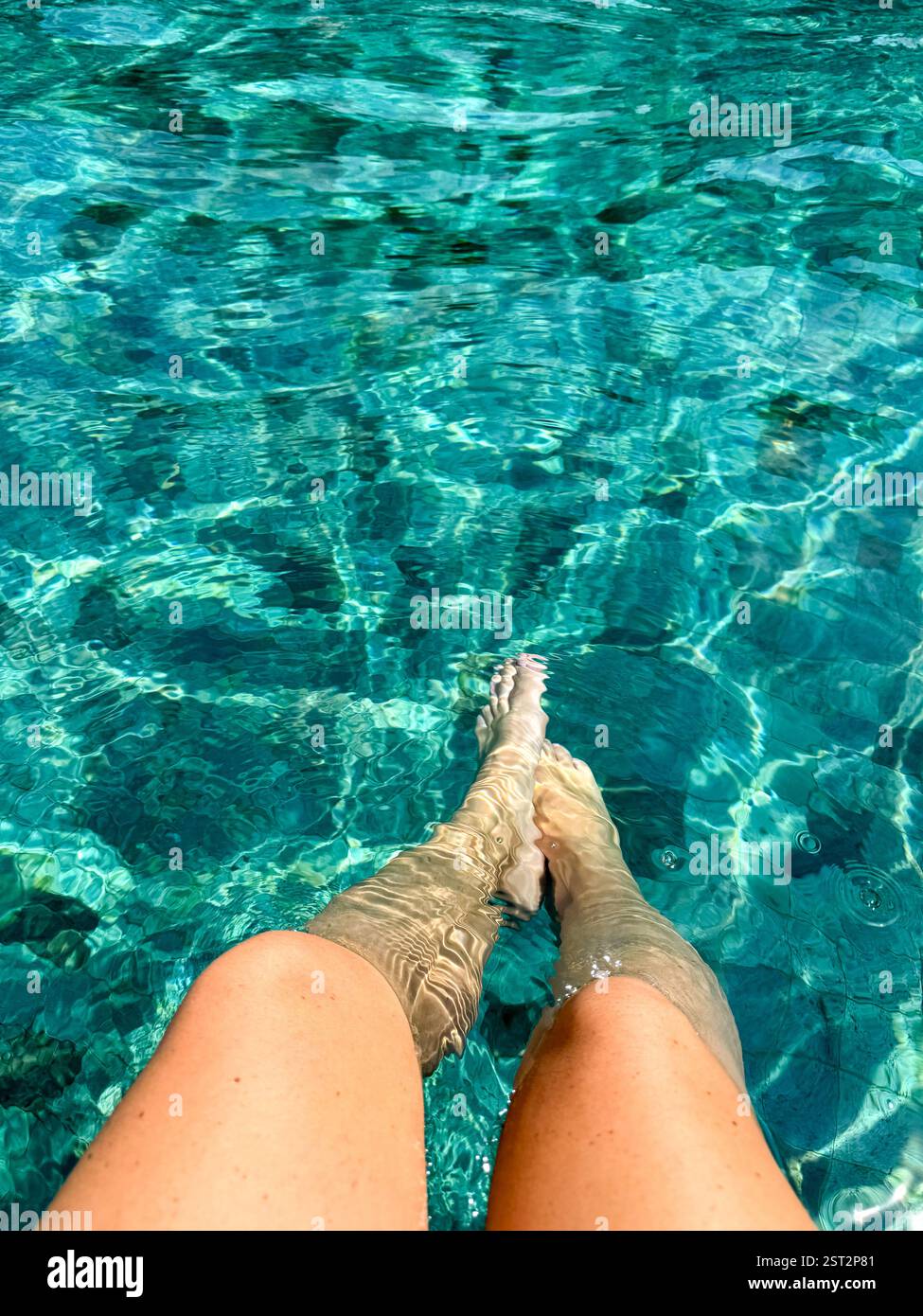 Relaxing Poolside Moment Two legs immersed in a turquoise-green tiled pool, capturing a moment of pure relaxation under the sun. - Smartphone Captured Stock Image