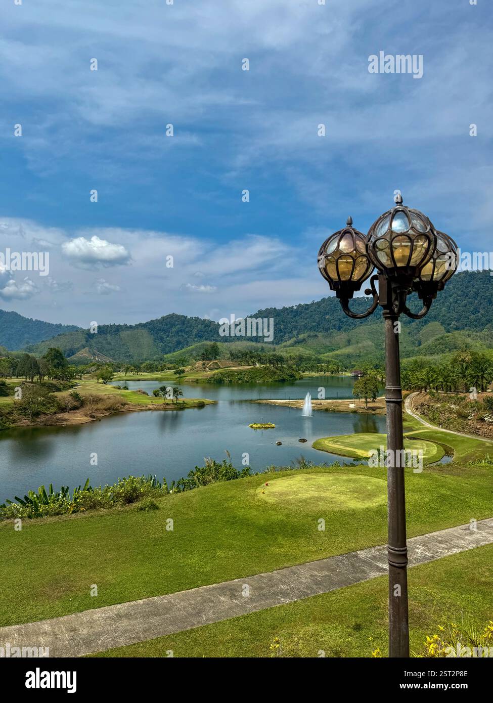 Vintage street lamp with a lake and green Golf hills view2 A vintage-style street lamp stands in front of a serene landscape featuring a peaceful lake - Smartphone Captured Stock Image