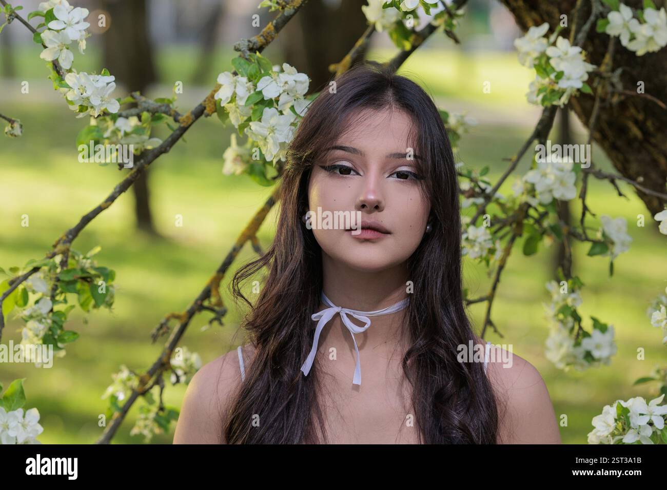 Beautiful Girl with long hair poses near white blossoming apple trees Stock Photo