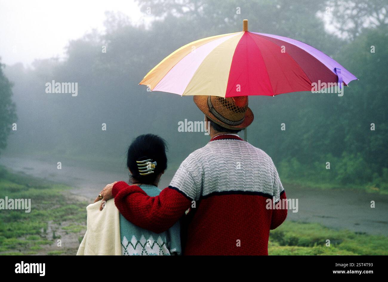 Old man and woman walking with umbrella in drizzling rain at ...