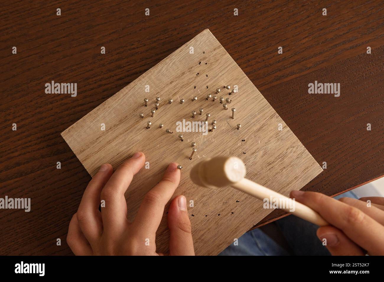Child hands working on a wooden craft project. Using a hammer, learning skills, and exploring creativity Stock Photo