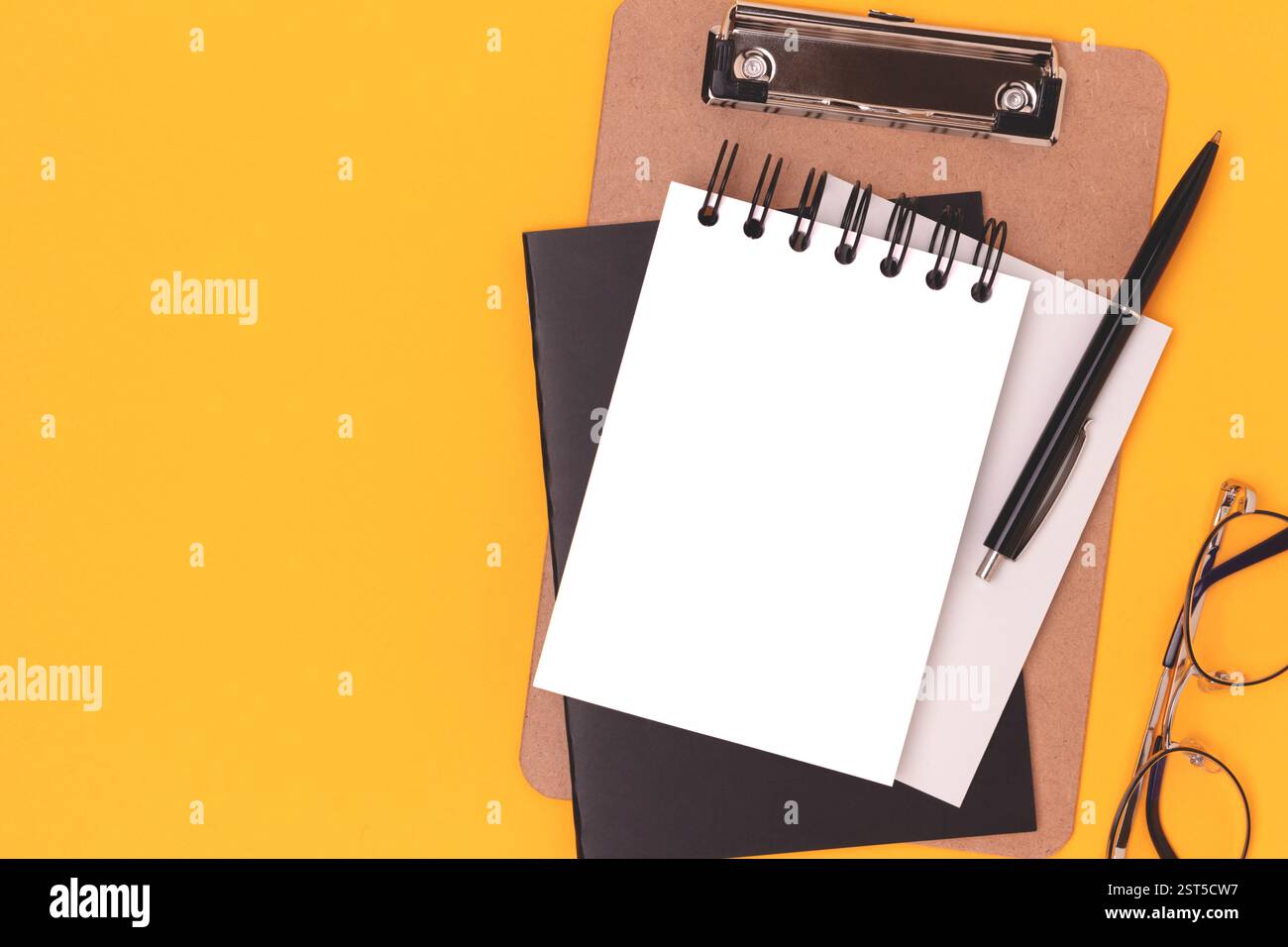 Workspace with blank notepad mockup, eyeglasses and stationery on a yellow background. Creative layout with place for text. Stock Photo