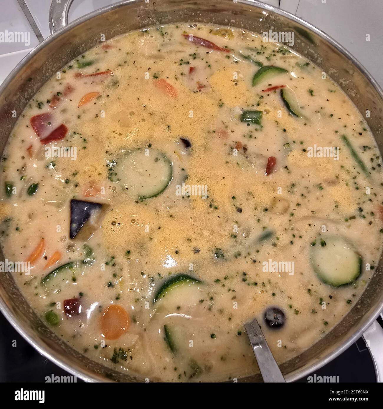 A delectable Creamy Vegetable curry Soup sits in a shiny Stainless Pot fluttering on the Stove Stock Photo