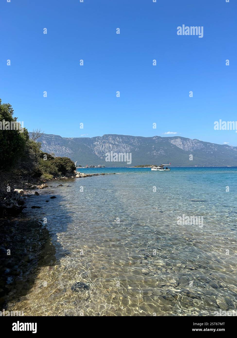 The crystal clear blue waters of the Mediterranean Sea surrounded by mountains and trees - Smartphone Captured Stock Image