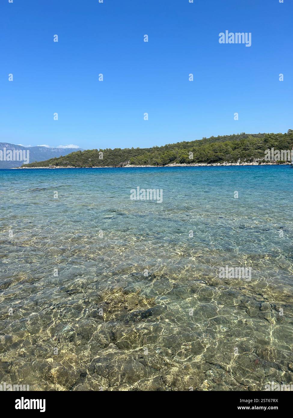 The crystal clear blue waters of the Mediterranean Sea against the tree covered mountains - Smartphone Captured Stock Image