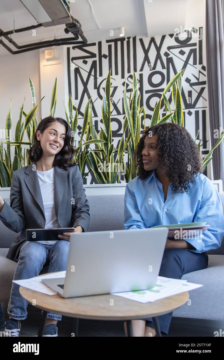 Two creative diverse colleagues sitting on sofa in office collaborating on project Stock Photo