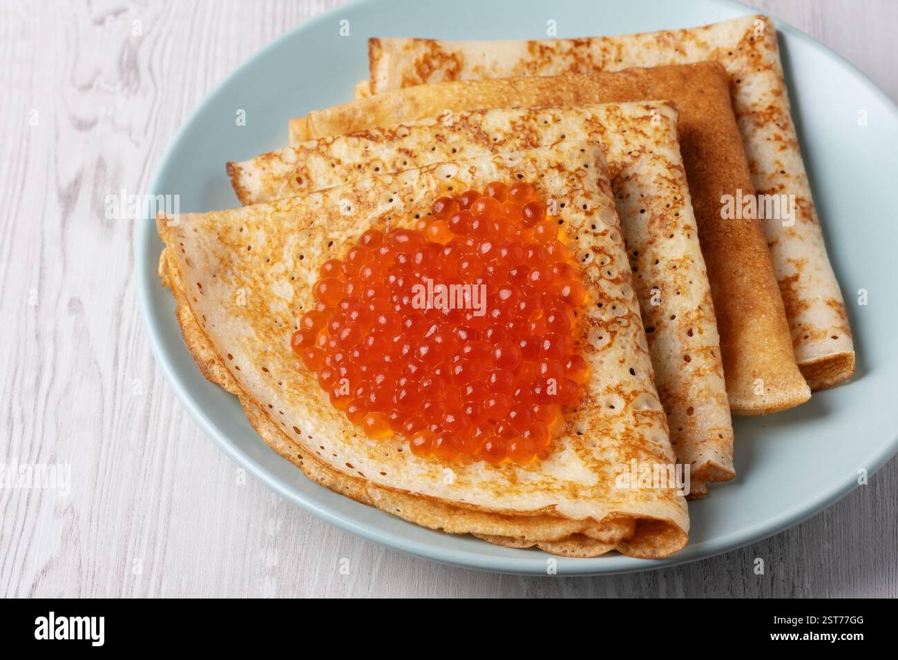 Savory crepes filled with fresh orange fish roe served on a light blue ...