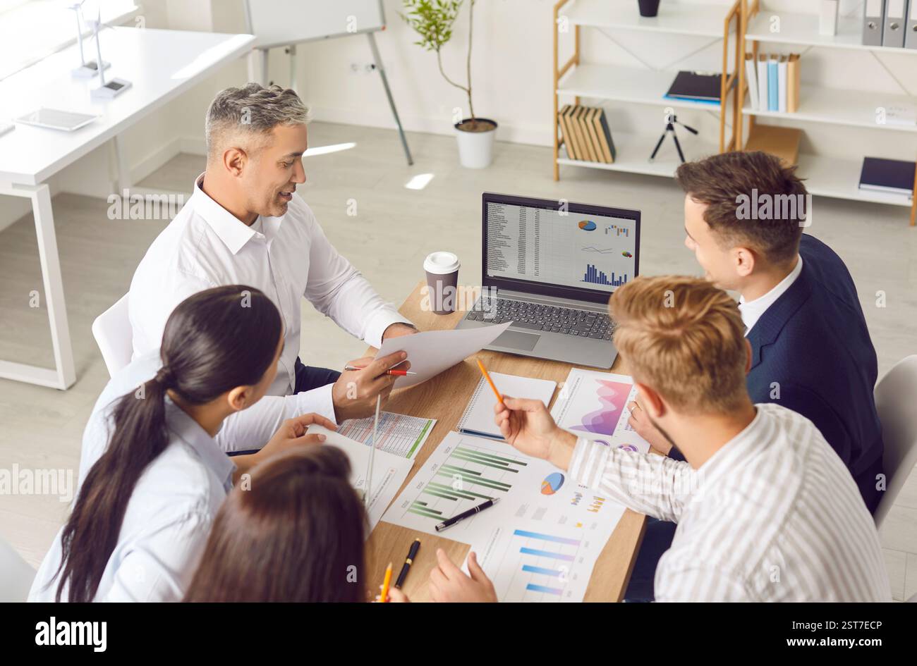 Business team sitting together at office table, doing data analysis, and using laptop Stock Photo