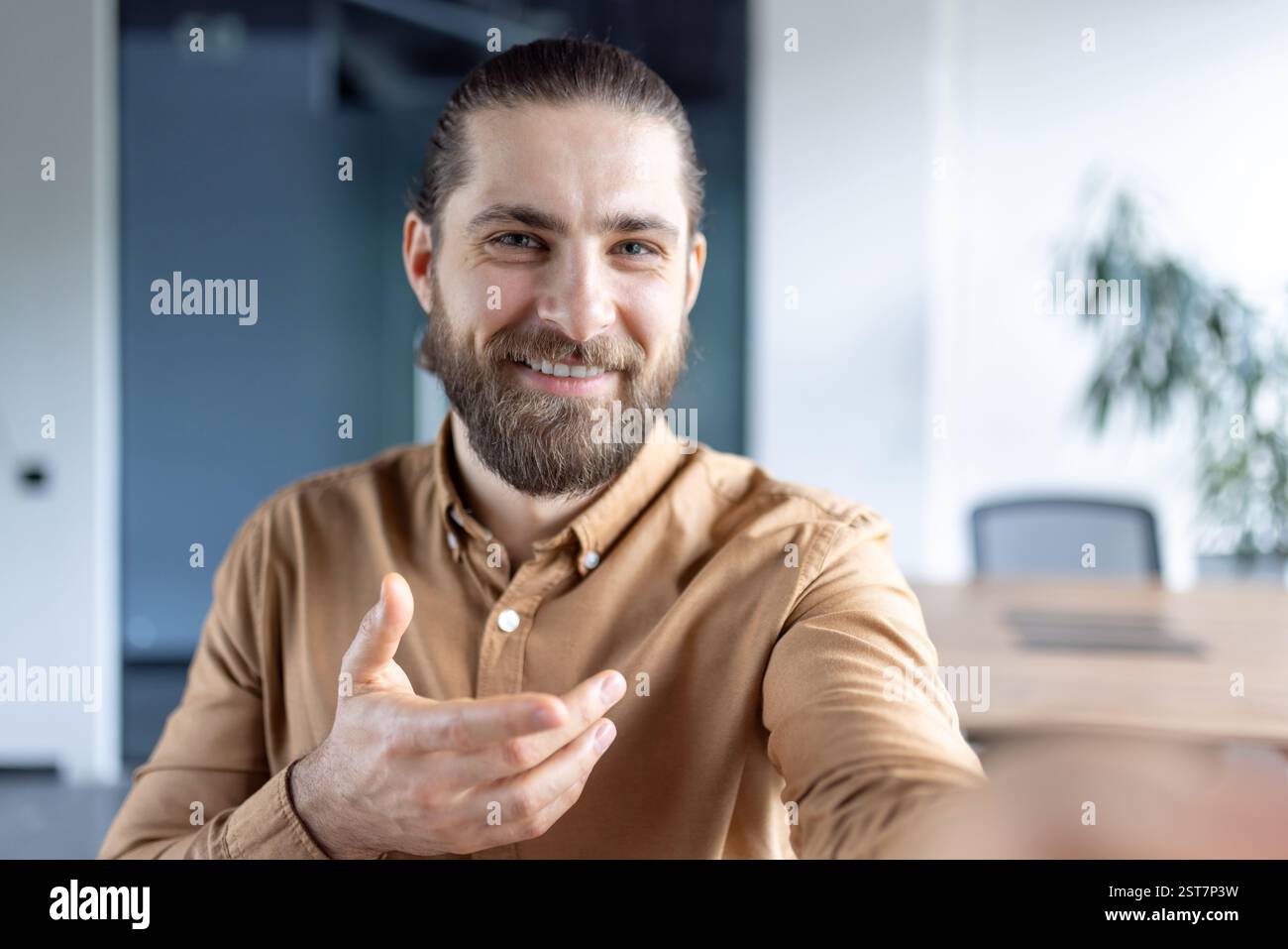 Webcam view, man inside office at workplace using smartphone app for video call, talking to colleagues and partners while sitting at desk. Stock Photo
