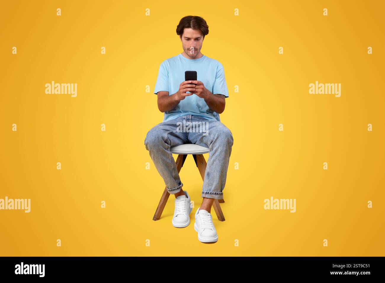 Focused guy using cellphone at studio, sitting on chair Stock Photo