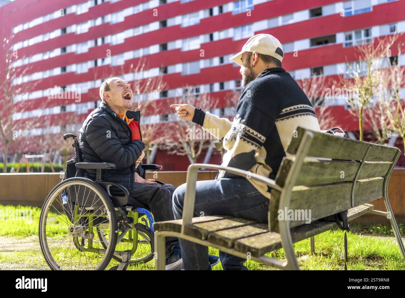 Two men enjoying time together in urban park, one using wheelchair ...